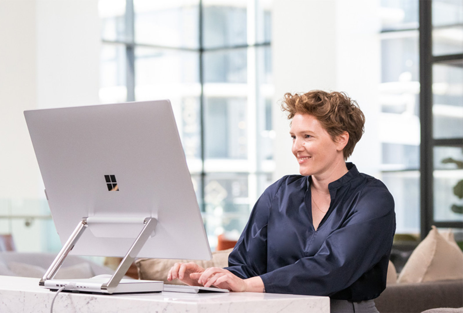 Woman sitting and typing on a Surface device with a large monitor