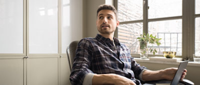A man in a plaid shirt sitting in a chair with a laptop.