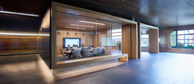 Mężczyzna w niebieskim fartuchu stoi przed laptopem, a w tle widać pionowe ściany w niebiesko-białe paski.