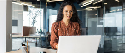 Seorang perempuan bekerja menggunakan laptop di ruang kantor modern.
