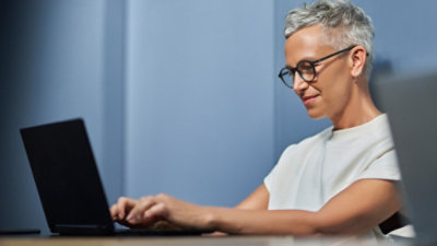 Personne assise à un bureau, tapant sur un ordinateur portable dans un espace de travail intérieur silencieux avec un arrière-plan bleu brut.