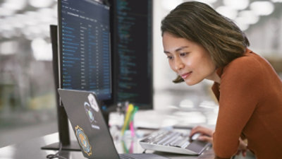 Persona trabajando en un portátil con monitores que muestran código