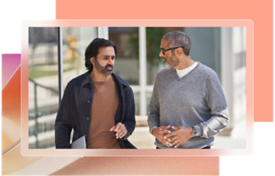 Двоє чоловіків розмовляють, один у коричневій сорочці, інший у сірому светрі.