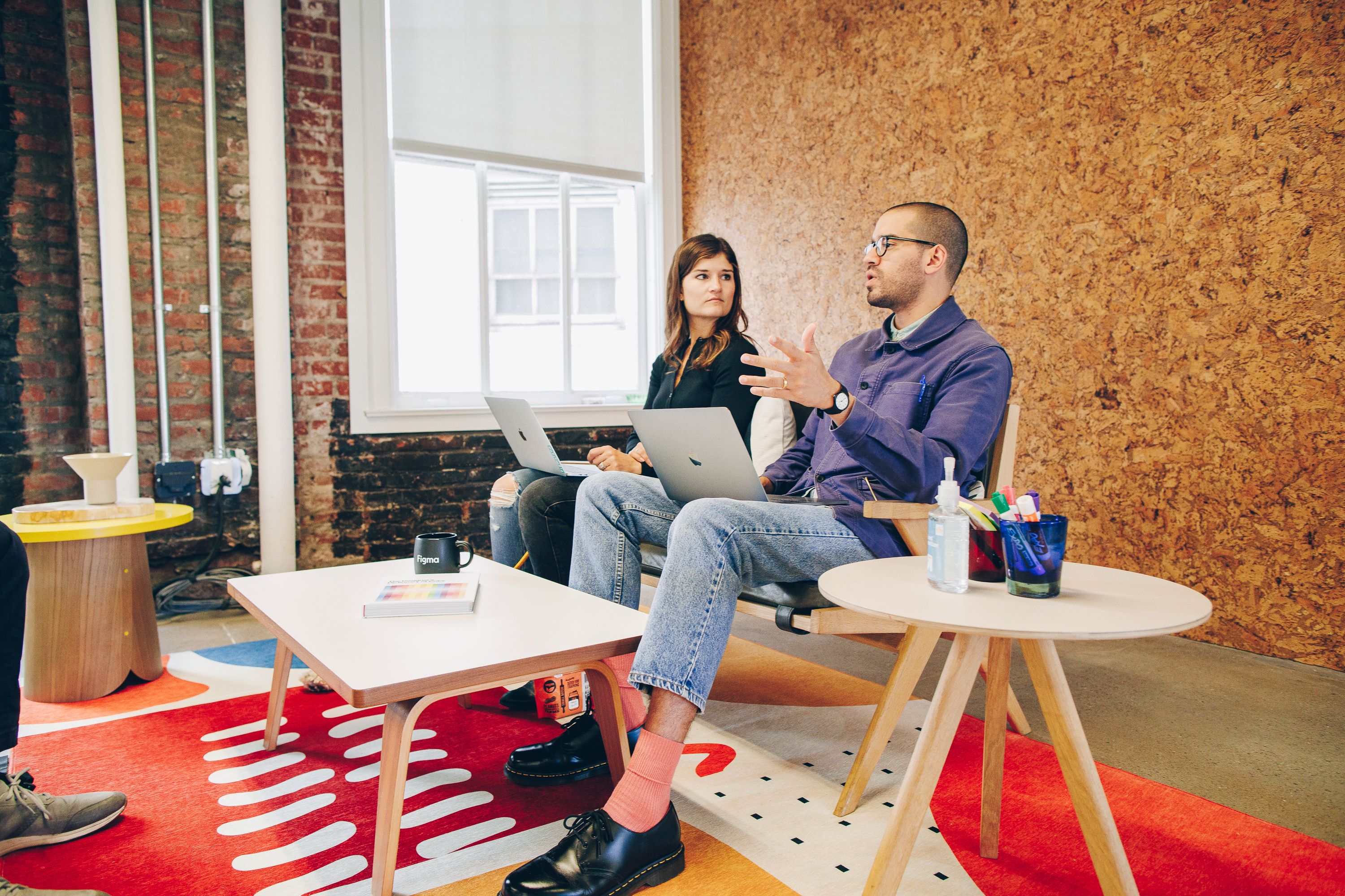 Two employees in an office room with their laptops talking to each other