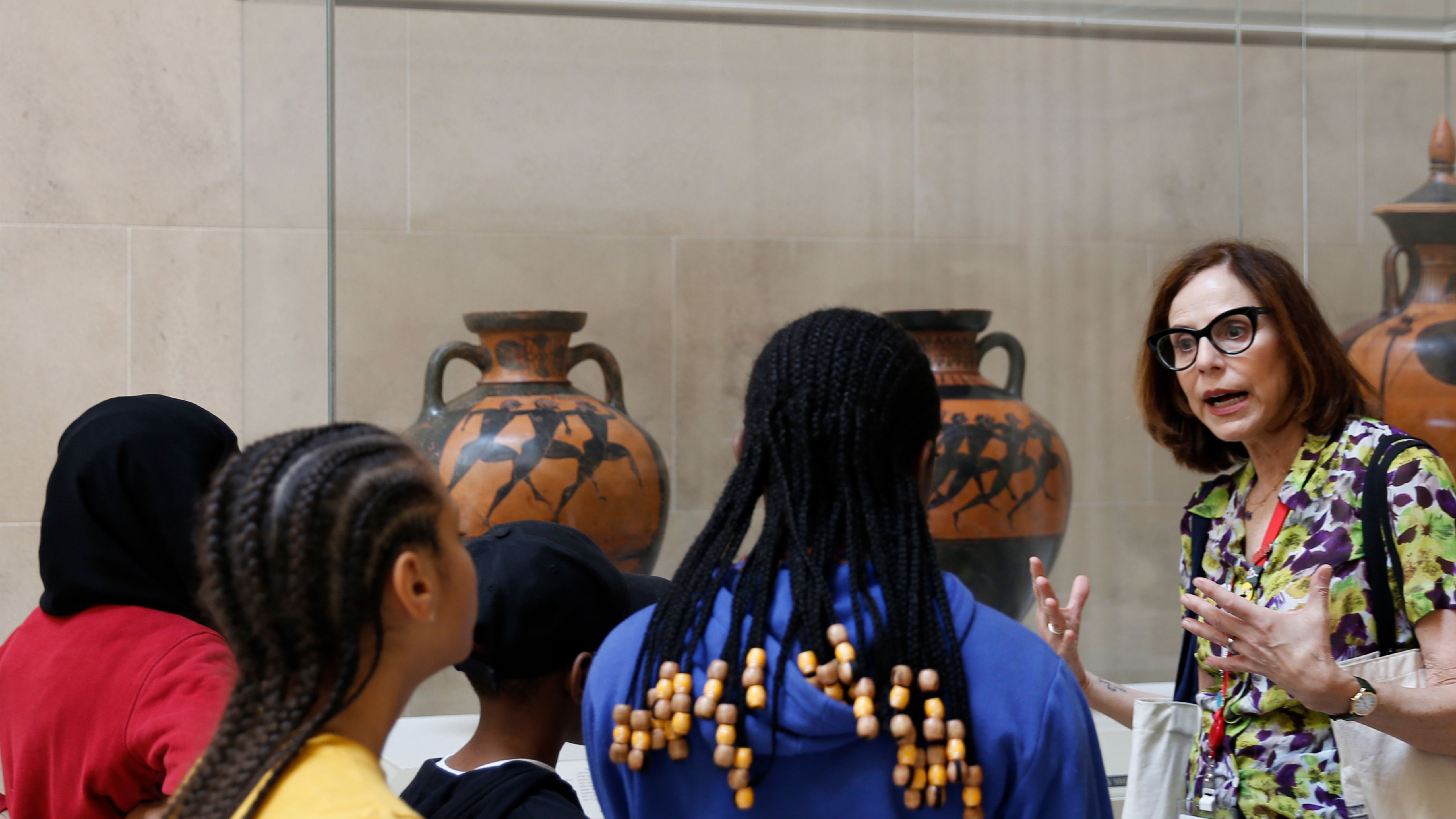 A group of young kids being led through the Greek and Roman Galleries by a docent.