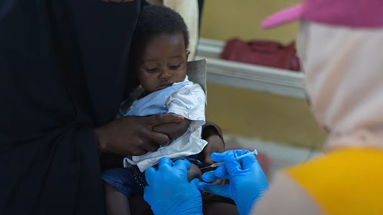 A curious baby sitting in his mother's lap, gets a vaccine shot.