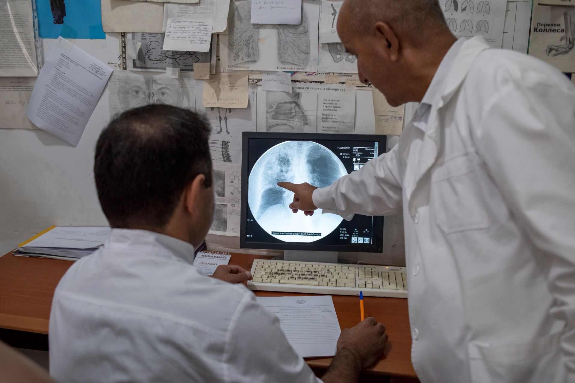 Two men in white lab coats look at an X-ray on a screen