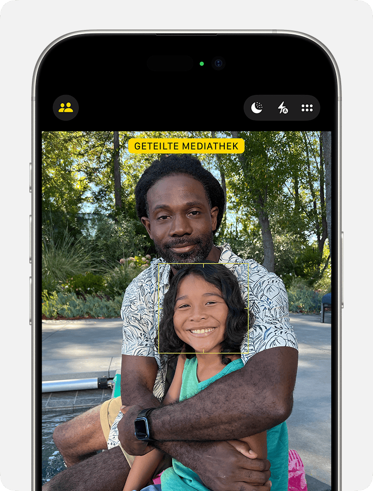 Ein iPhone mit der Taste „Geteilte Mediathek“ befindet sich oben auf dem Display in der Kamera-App.