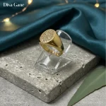 About Luxury 18K gold plated oval signet ring with pavé crystal center resting on a dark teal silk cloth background