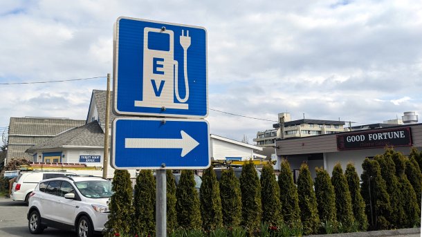 Ein Verkehrsschild weiĂźt den Weg zu einer Ladestation fĂĽr Elektroautos. In dem Foto zeigt der Pfeil auch auf ein Restaurant namens "Good Fortune".