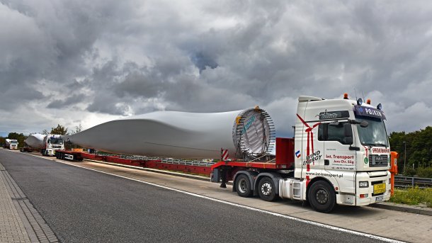 Drei Schwertransporte stehen an einer Straße und haben Bauteile für Windräder auf ihren Anhängern.