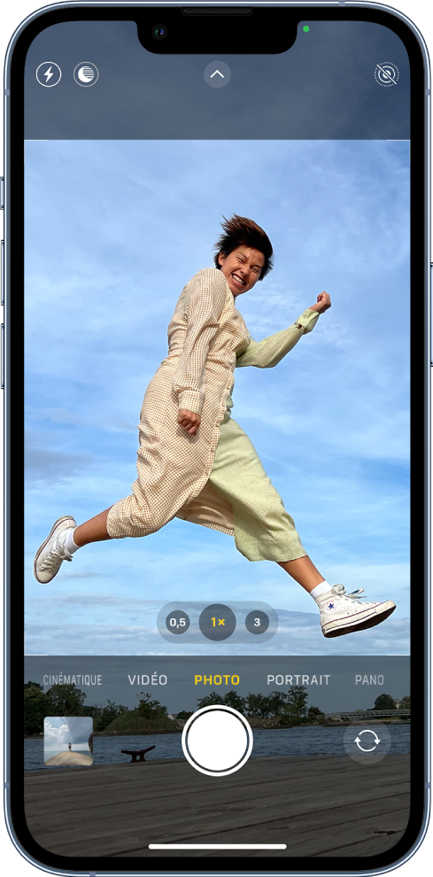 L’écran Appareil photo en mode Photo, avec les autres modes à gauche et à droite sous le viseur. Les boutons pour le flash, le mode Nuit, les commandes de l’appareil photo, le format ProRaw et le mode Live Photo apparaissent en haut de l’écran. En dessous des différents modes d’appareil photo, de gauche à droite, se trouvent le bouton « Visualiseur de photos et vidéos », le bouton « Prendre une photo » et le bouton « Sélecteur de caméra - face arrière ».