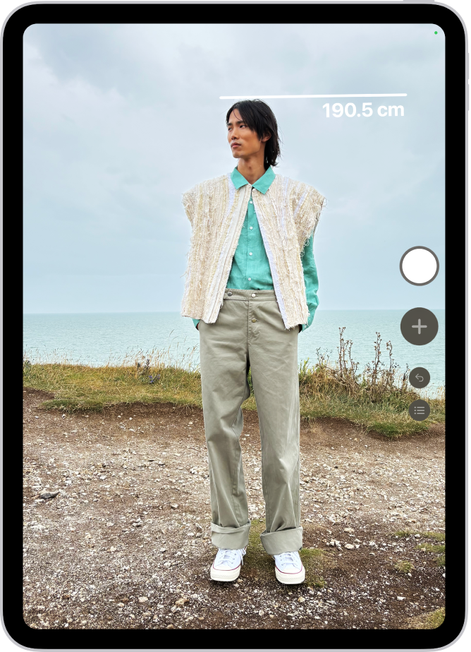 Meranie výšky osoby v apke Meradlo. Nameraná výška sa zobrazuje v hornej časti hlavy osoby. V blízkosti pravého dolného rohu je tlačidlo Odfotiť, pomocou ktorého môžete zhotoviť snímku merania. Hore sa nachádza zelený indikátor Kamera sa používa.