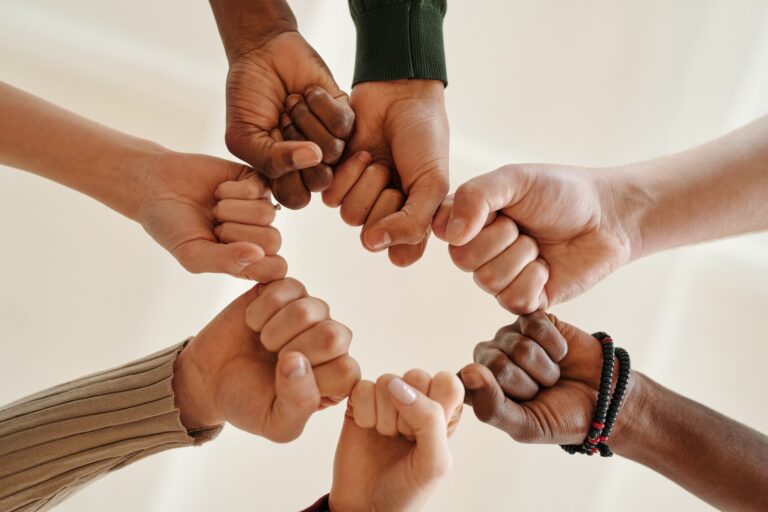 hands seen from below, extended from many directions to meet in a circle of fists, a symbol of solidarity