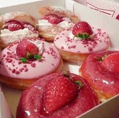 four donuts with pink icing and strawberries in a box