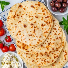 three pita breads on a blue and white plate with cherry tomatoes