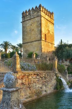 an old castle with a fountain in front of it and a fence around the pond