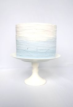 a white cake with blue frosting sitting on top of a plate in front of a wall