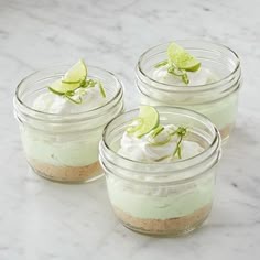 four small mason jars filled with whipped cream and topped with limes on a marble surface