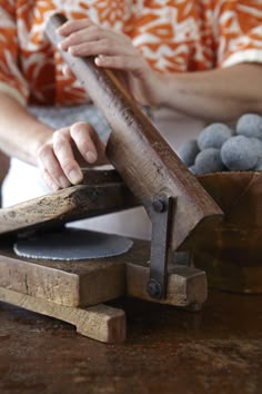 a woman is using a hand sander on a wooden table with rocks in the background
