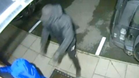 Two people running into a home front door as seen by home security CCTV. The men are entirely covered in black and blue outfits, hoods, gloves and masks.