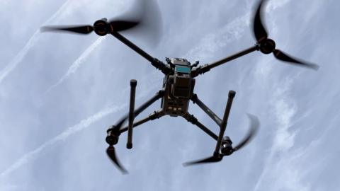 A laser scanning drone is seen flying against a blue sky.