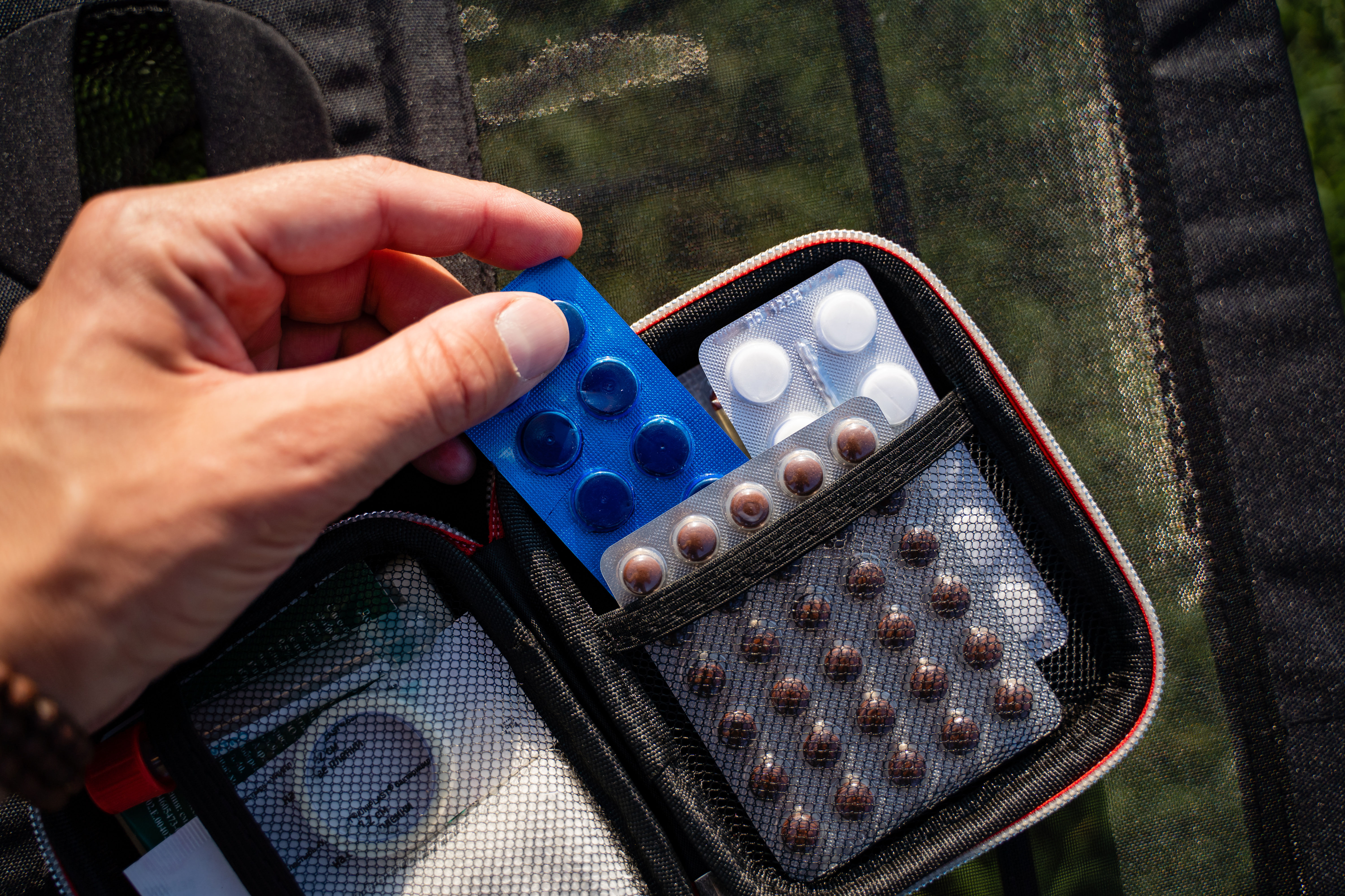 A hand is holding various medications that are available in a first aid kit while being outdoors