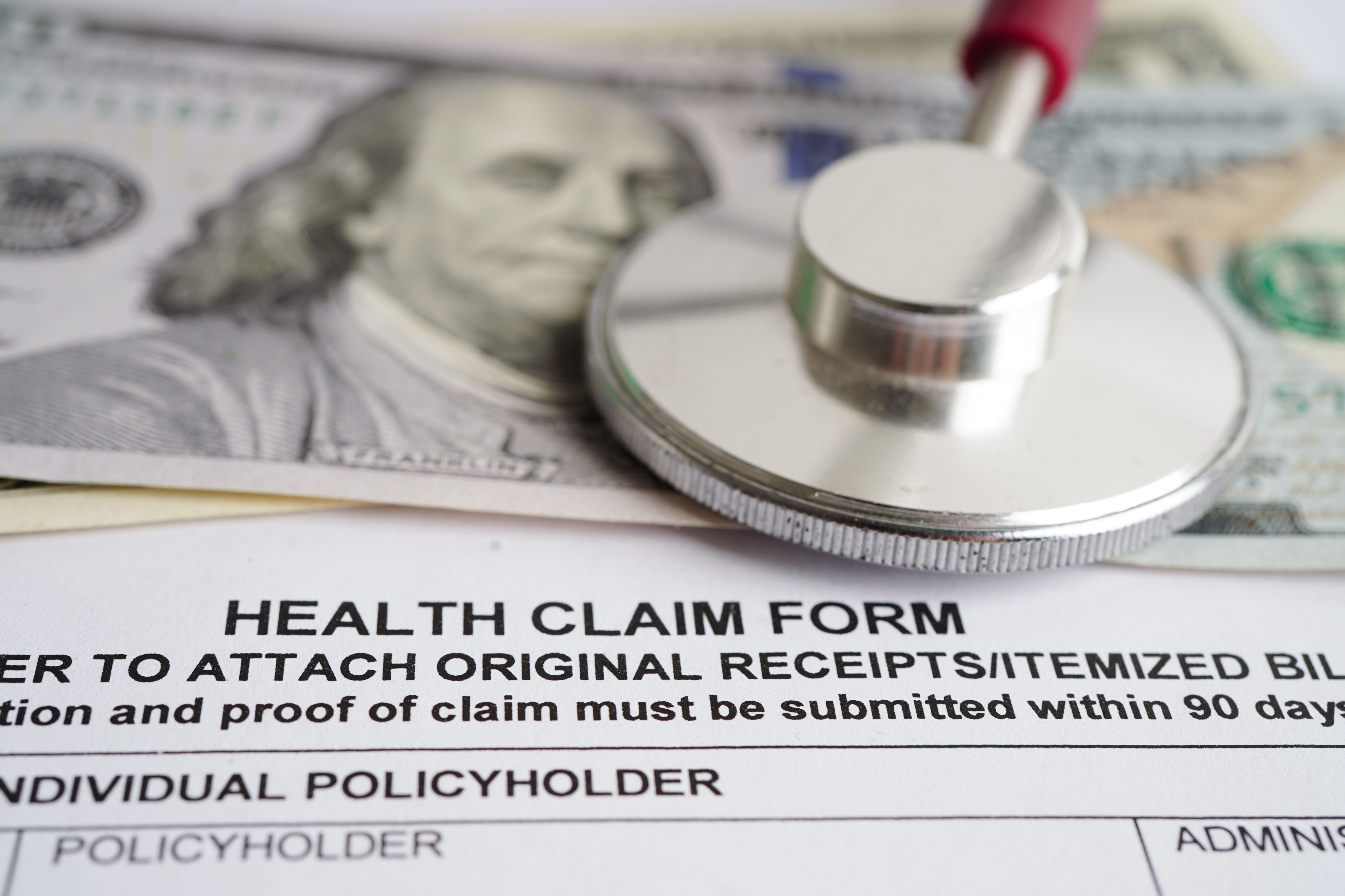 Health claim form with stethoscope and 100 dollar banknotes for medical insurance concept