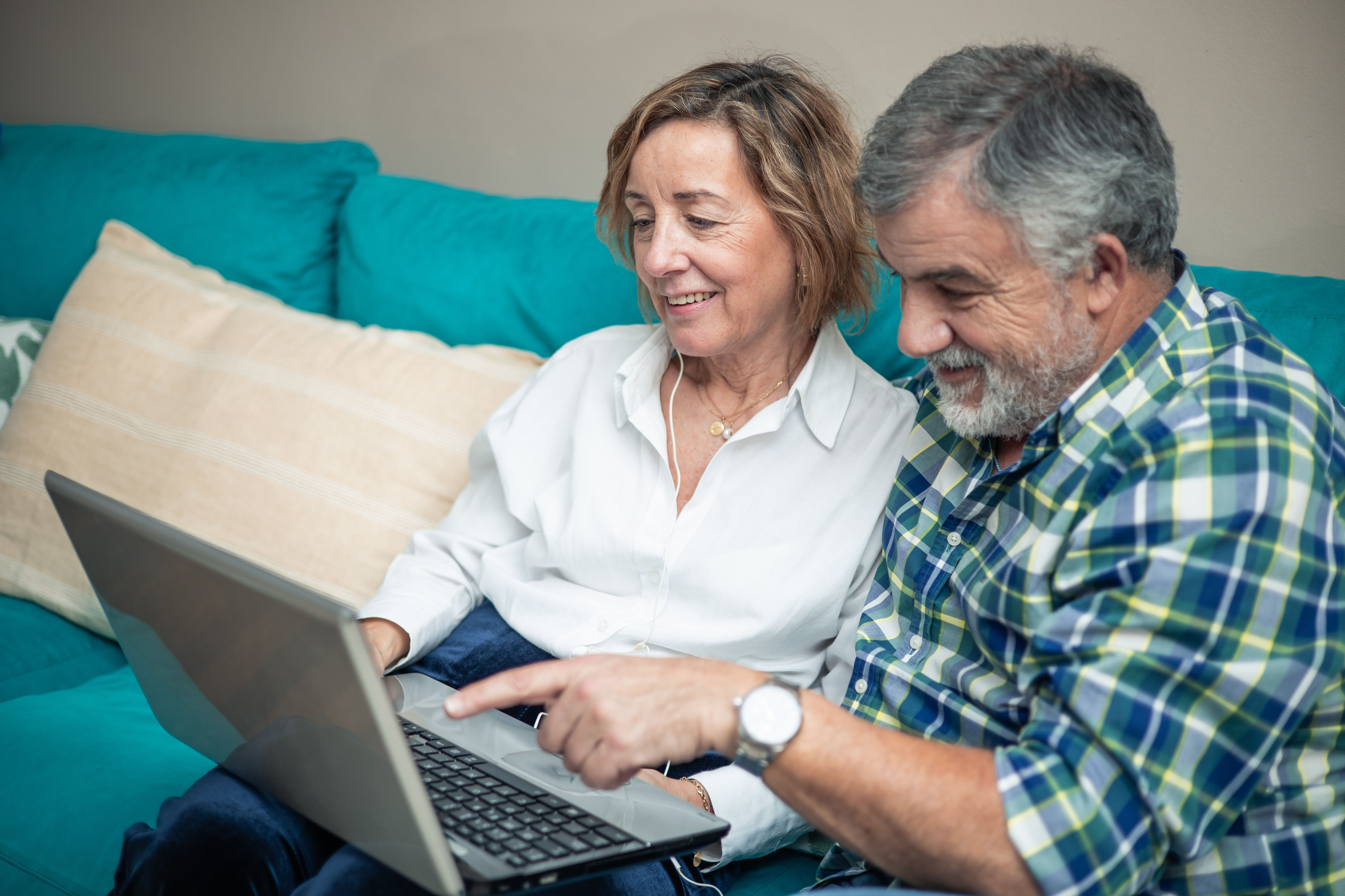 A retired couple sitting on sofa and looking at their laptop screen