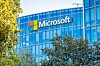 Microsoft logo on a blue glass office building partly obscured by trees