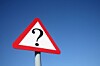 A triangular road sign with a question mark on a pole against a blue sky.