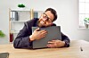 Man in glasses rests his head on a closed laptop at a desk in a bright office