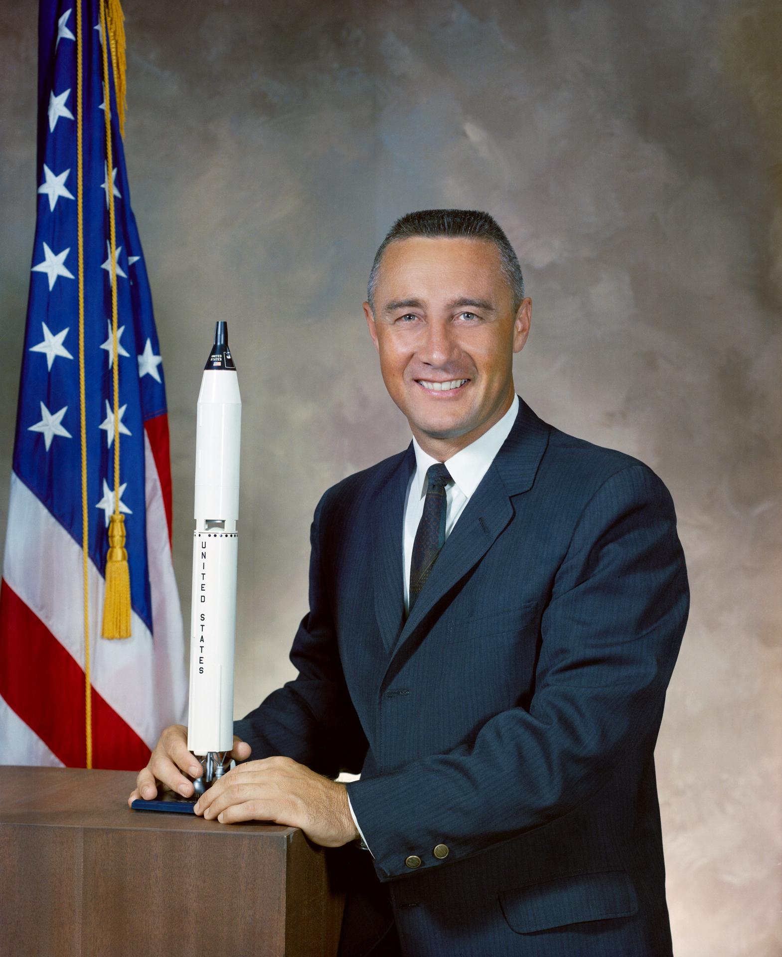 Official portrait of Gus Grissom with model shuttle in front of US flag
