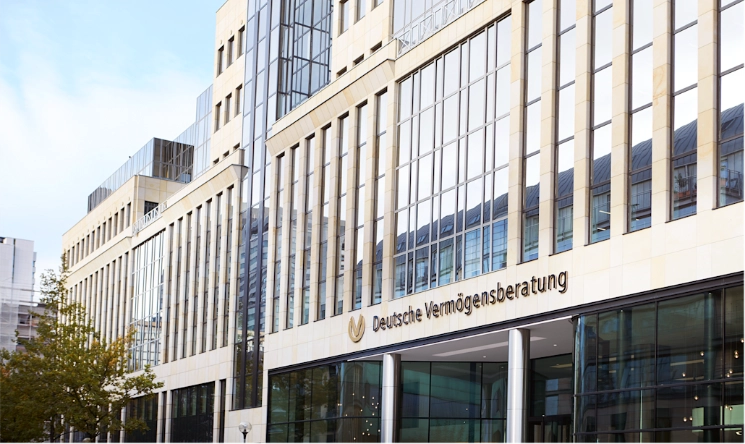 Modern office building with large glass windows and beige stone facade. Sign reads "Deutsche Vermögensberatung".