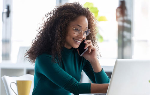 Person smiling while chatting on the phone in front of laptop.