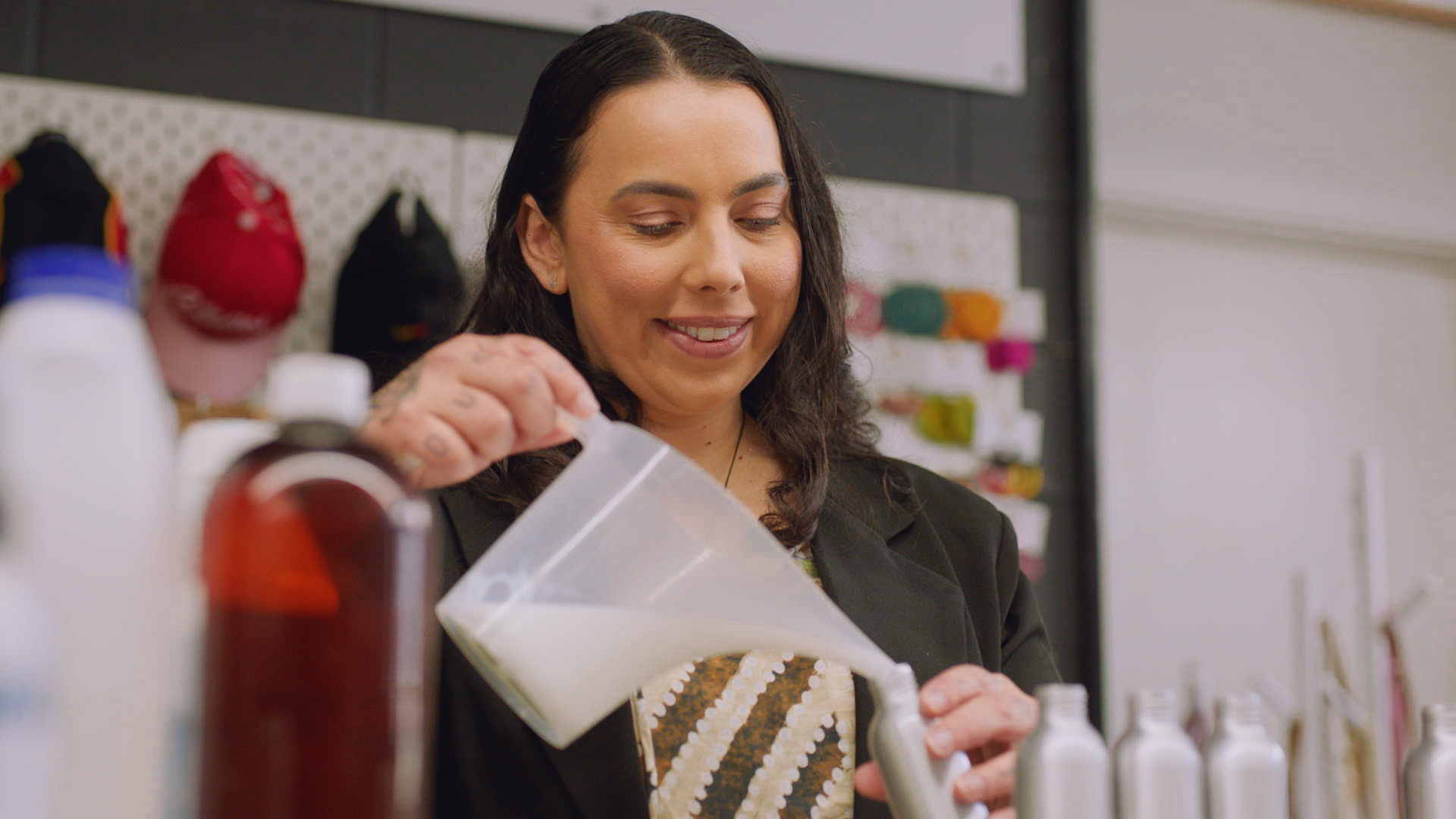 Person in dark jacket, smiling while pouring a white liquid into a container.