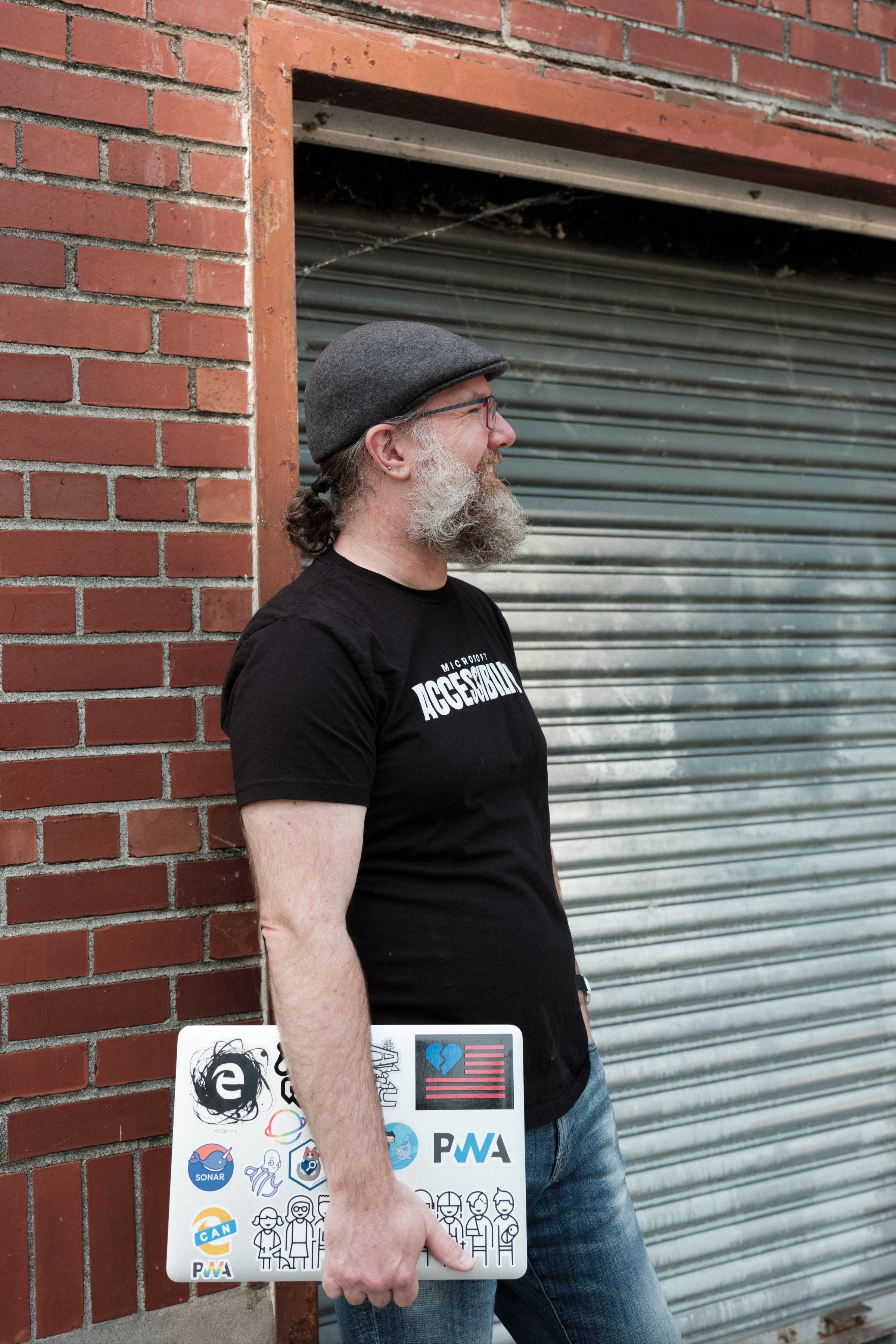 Turned to the side and smiling into the distance, Aaron holds a laptop covered in stickers.