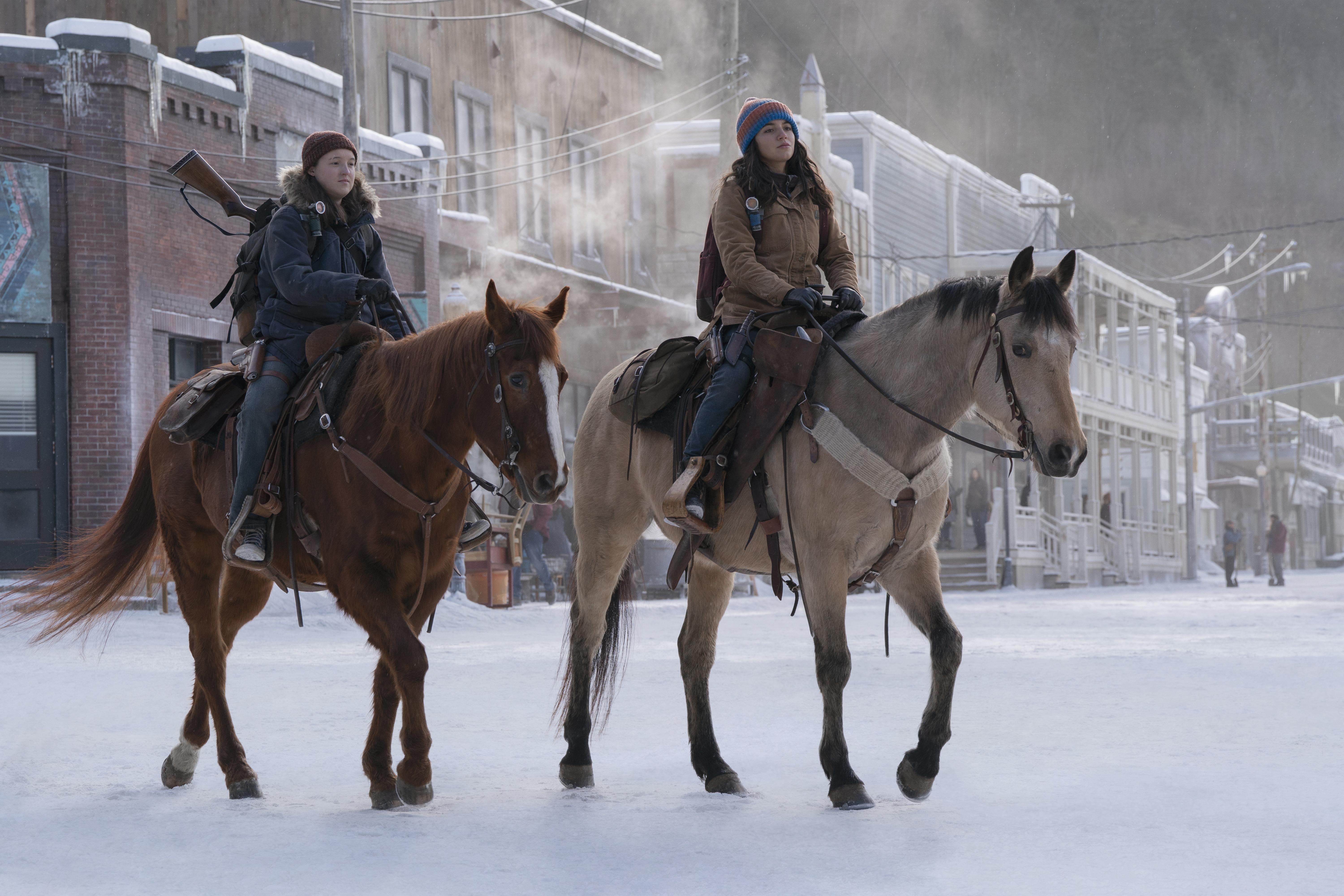 The Last of Us Bella Ramsey as Ellie and Isabela Merced as Dina in The Last of Us, riding horses through the snow
