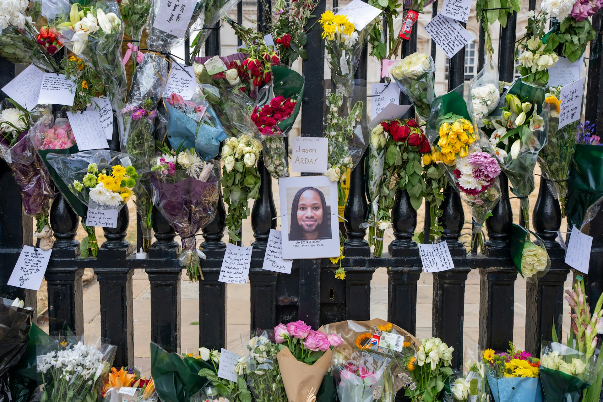 A photo of a young Black man with dreadlocks affixed to a black fence, surrounded by colorful flowers and handwritten notes.
