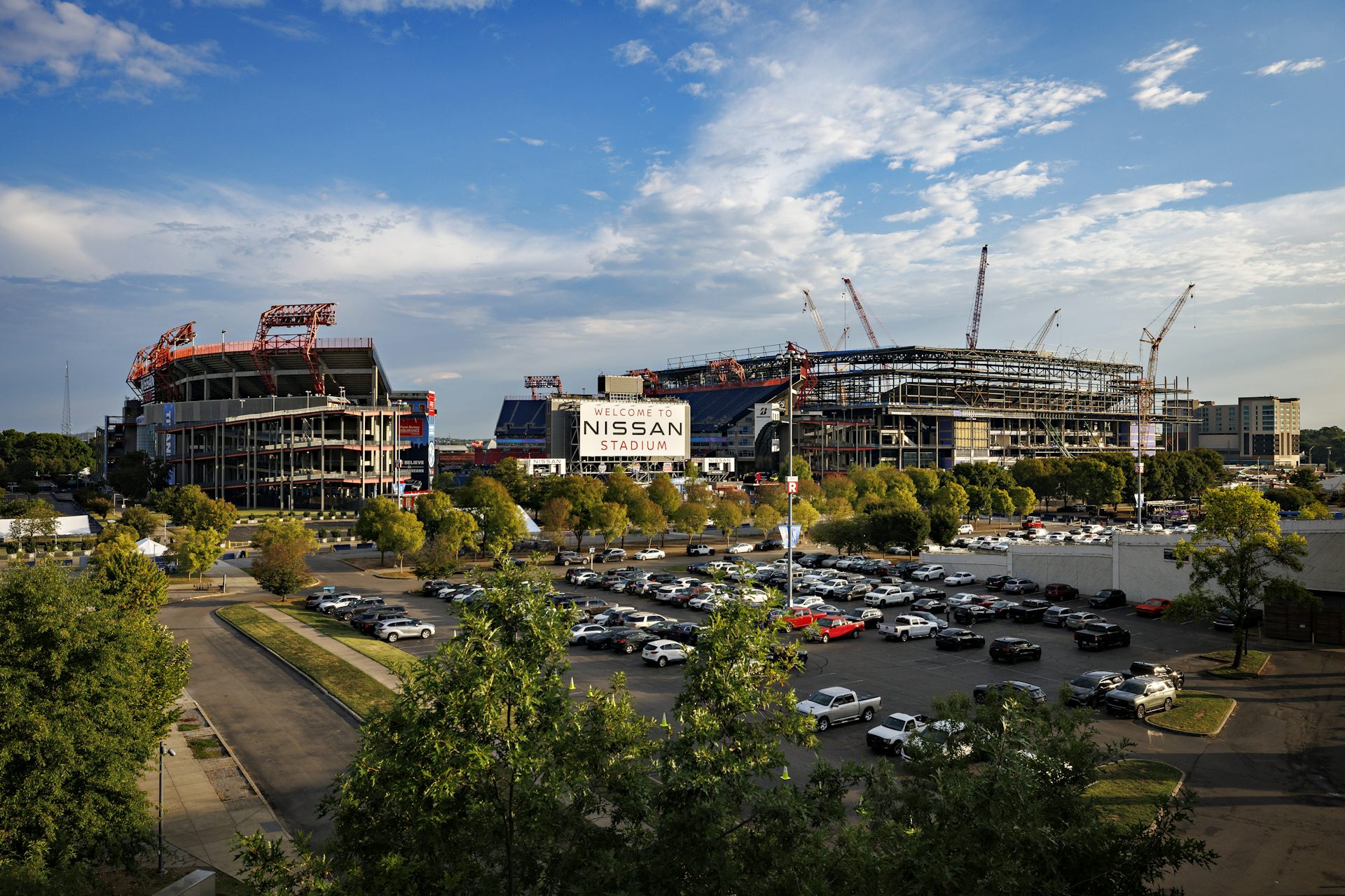 View of a parking lot in front of a large football stadium, and another stadium under construction to its right. 