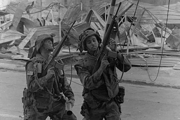Two soldiers from the 4th Battalion, 6th Infantry, 5th Infantry Division (Mechanize), search for a sniper hidden in a building near the destroyed Panamanian Defense Force headquarters during the second day of Operation Just Cause. (National Archives/Photographer's Hand 1st Class Elliott)