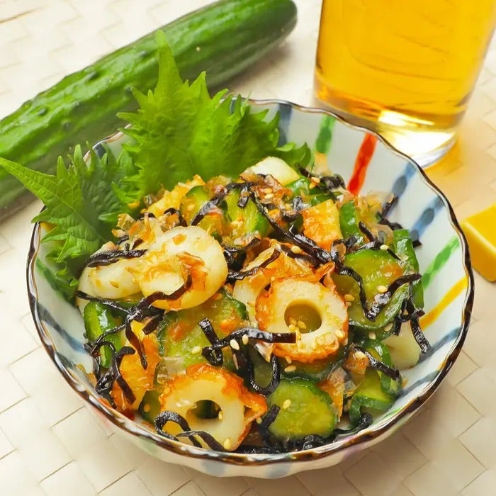 きゅうり、ちくわ、昆布の和風サラダが器に盛られています。背景にはきゅうりと飲み物が置かれています。