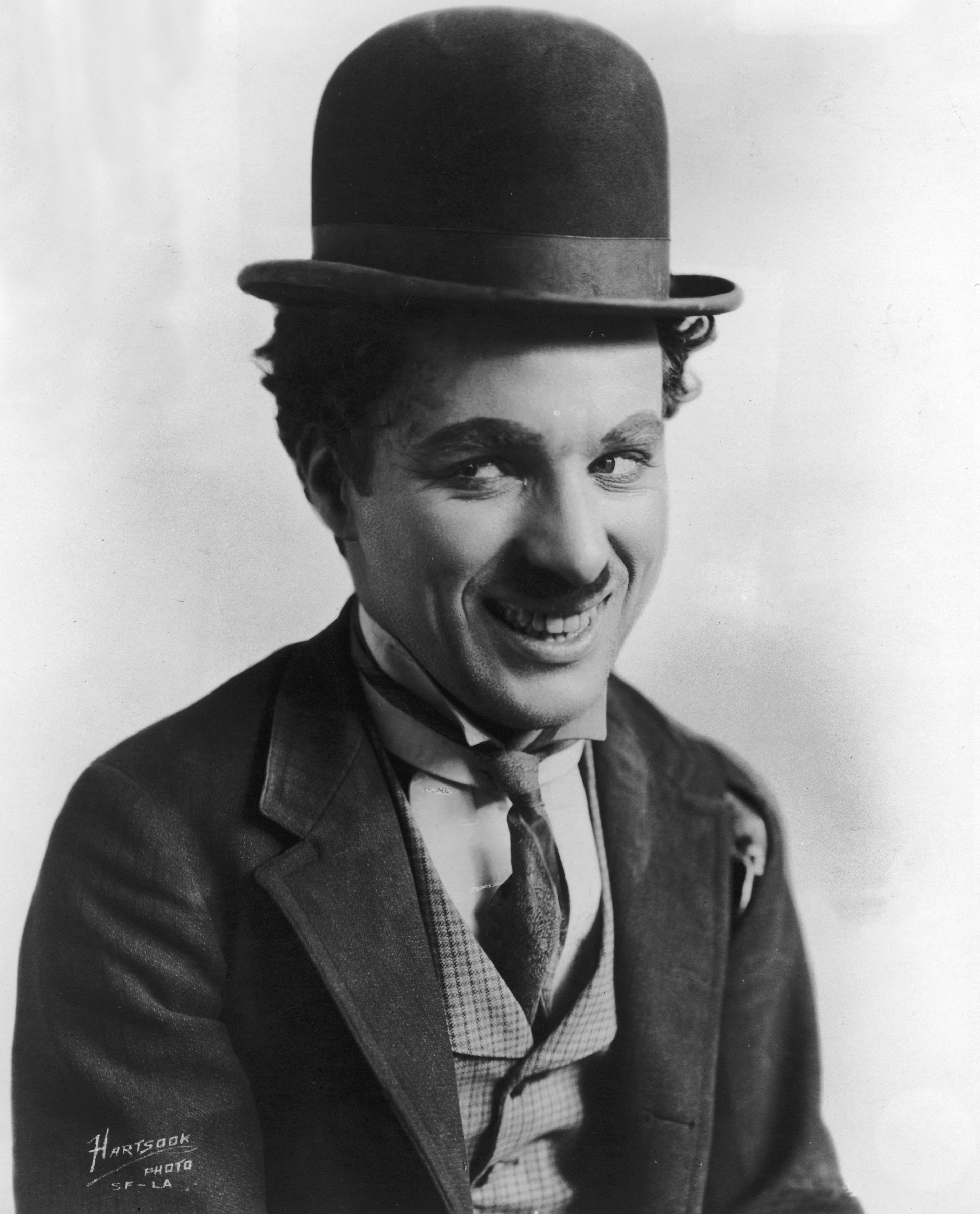 Person in bowler hat and suit looks at the camera with a subtle smile