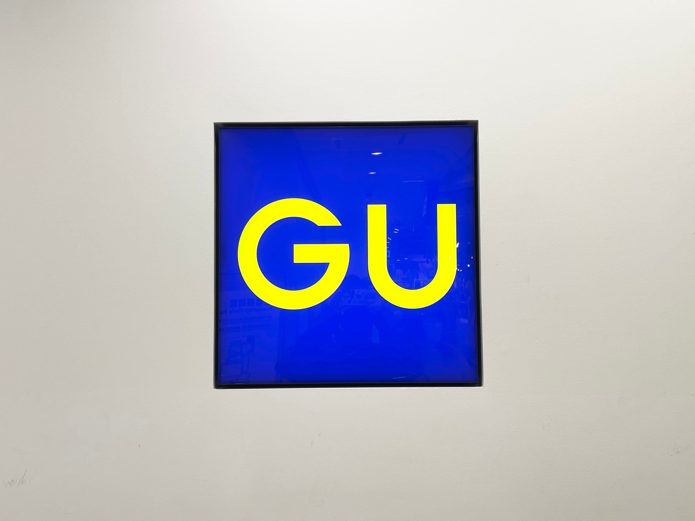 A square sign with bold yellow "GU" letters on a blue background