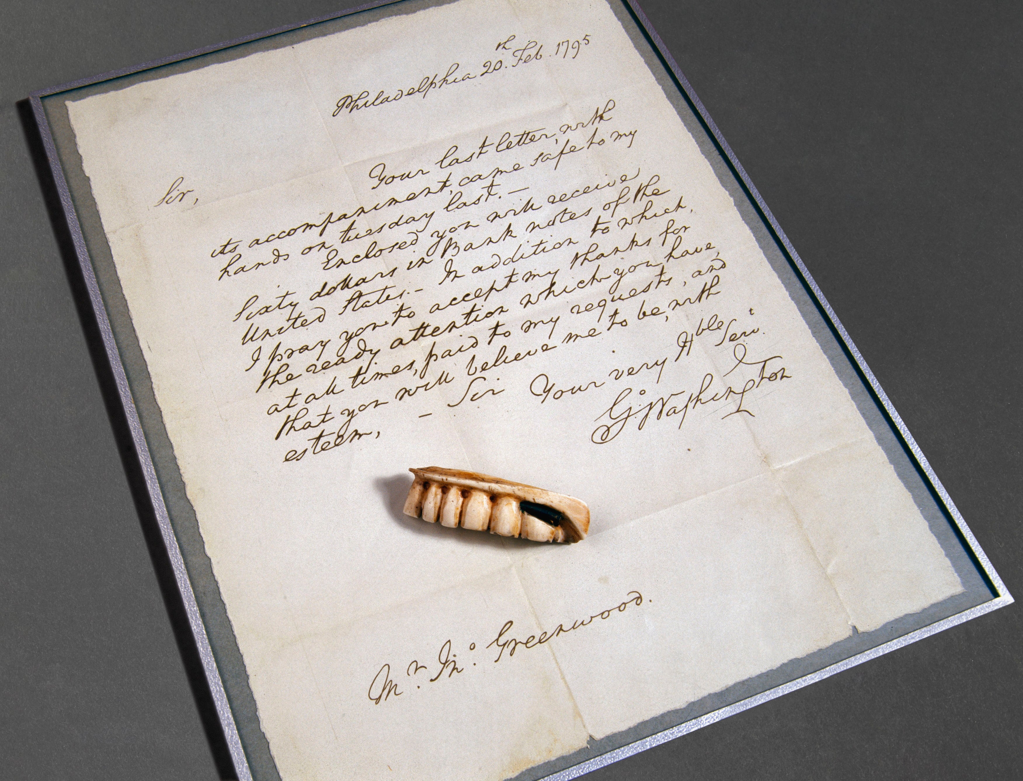 A handwritten letter from 1795 is displayed with a set of dental prosthetics, possibly illustrating historical dental practices