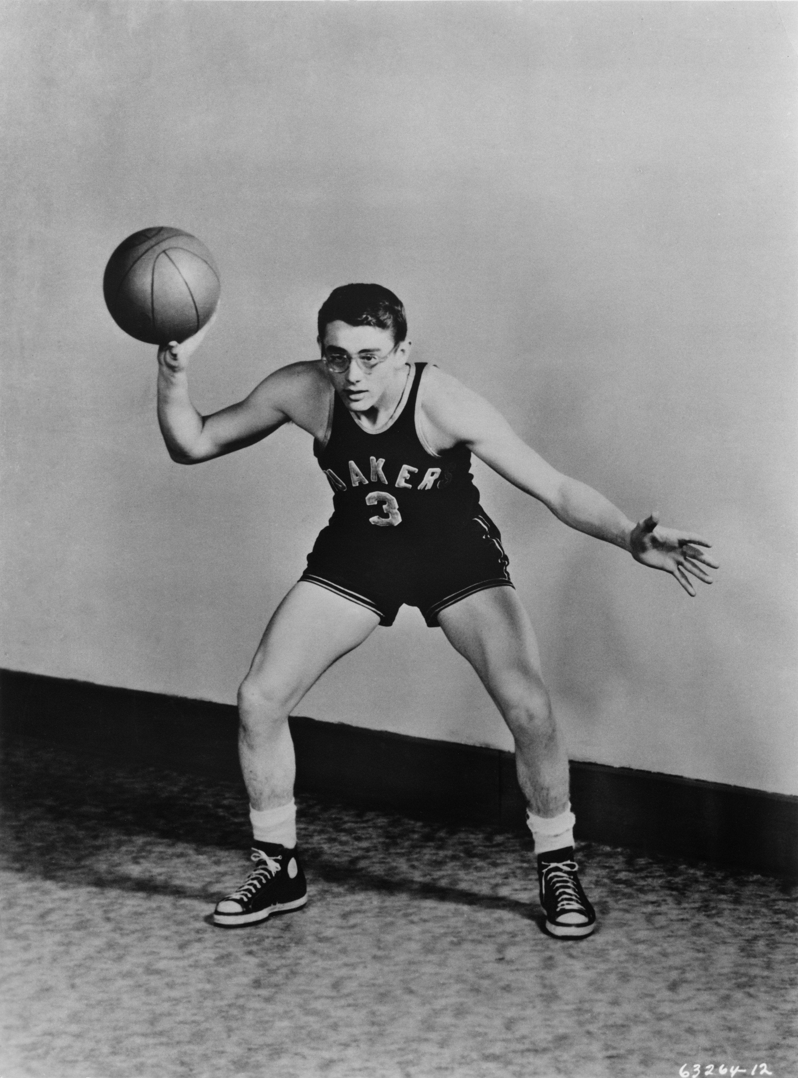 Vintage basketball player in action pose, wearing a Lakers uniform and sneakers, holding a basketball with one hand ready to dribble