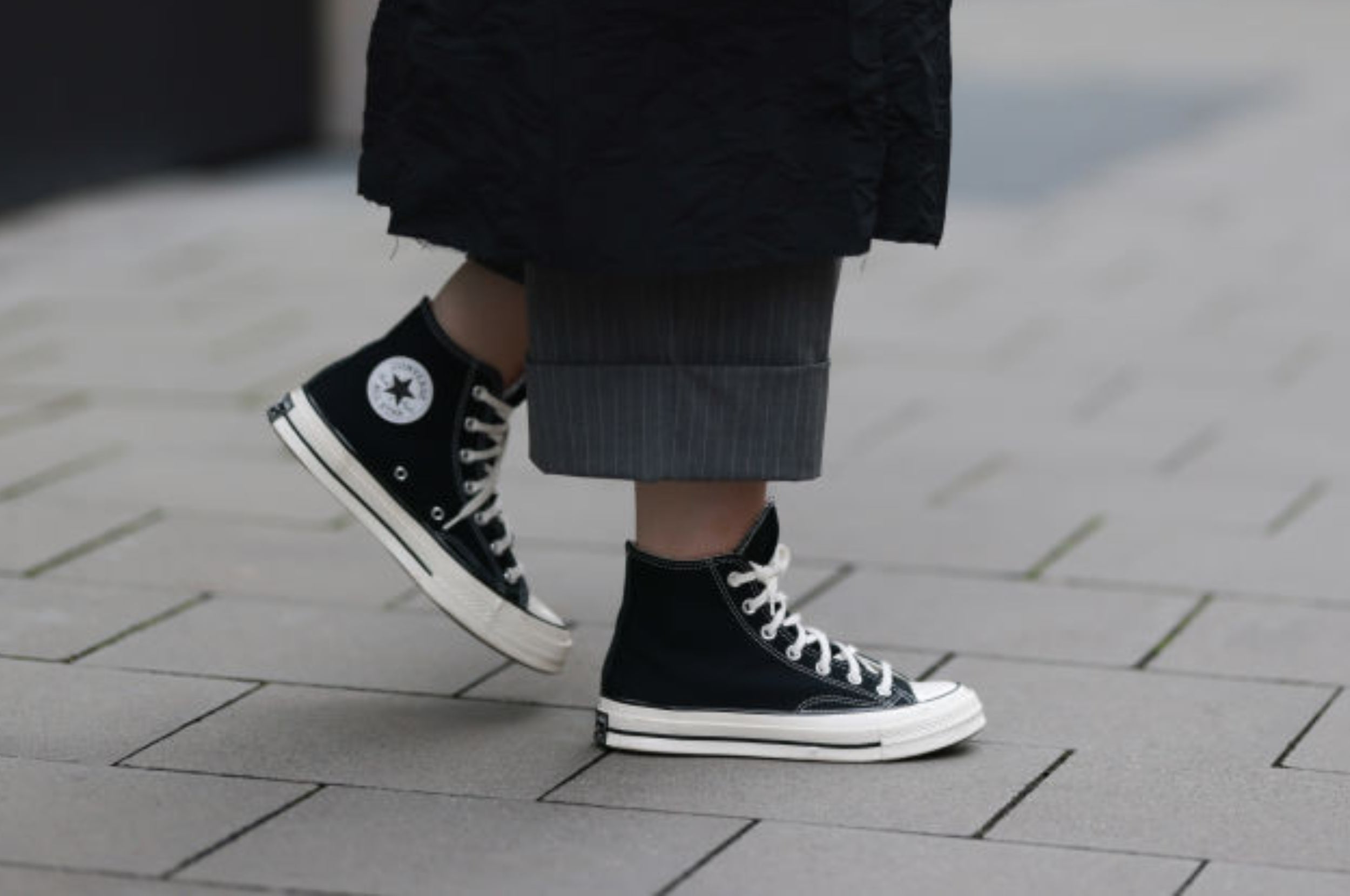 Person wearing black high-top sneakers with star logo on a paved street, visible from ankle to mid-calf with long dark coat