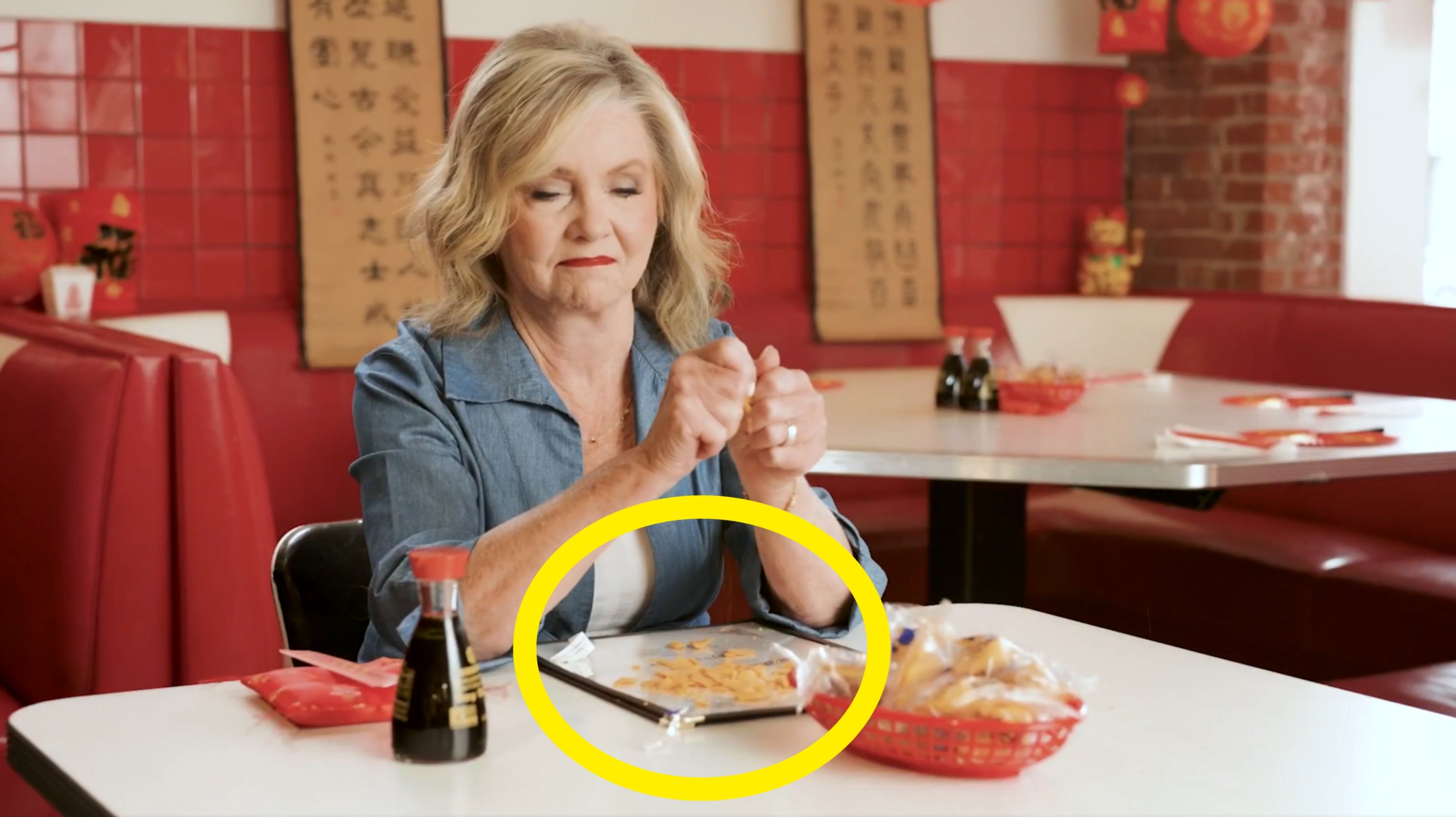A person in a diner, seated at a table with fortune cookies, appears to be opening a plastic wrapper