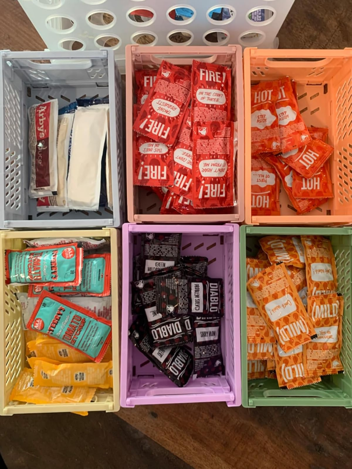 Assorted condiment packets neatly organized in bins, mainly containing hot sauce from a popular fast-food chain