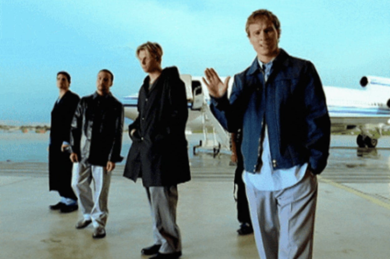 Five people stand in front of a jet, dressed in casual, slightly oversized outfits from the late 1990s or early 2000s